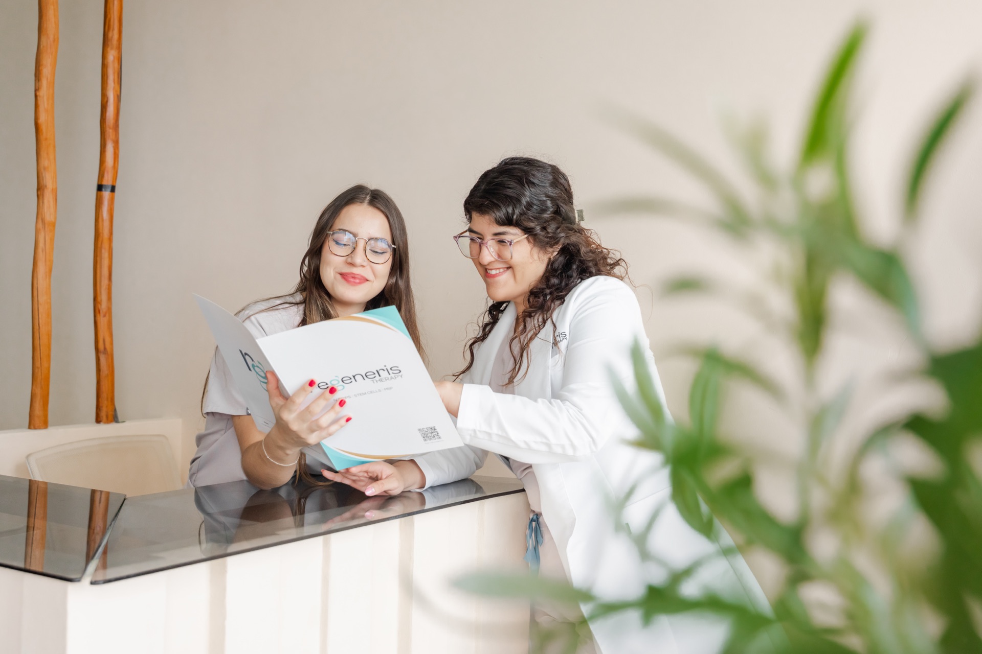 Two women at the Regeneris clinic reception desk reviewing a document together